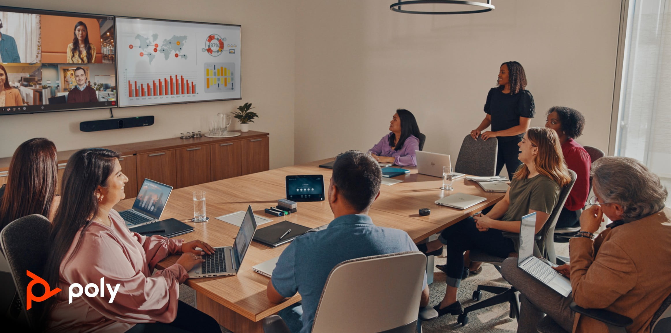  A team meets around a large conference table, with remote colleagues joining from a video feed displayed on an HP wall-mounted monitor.