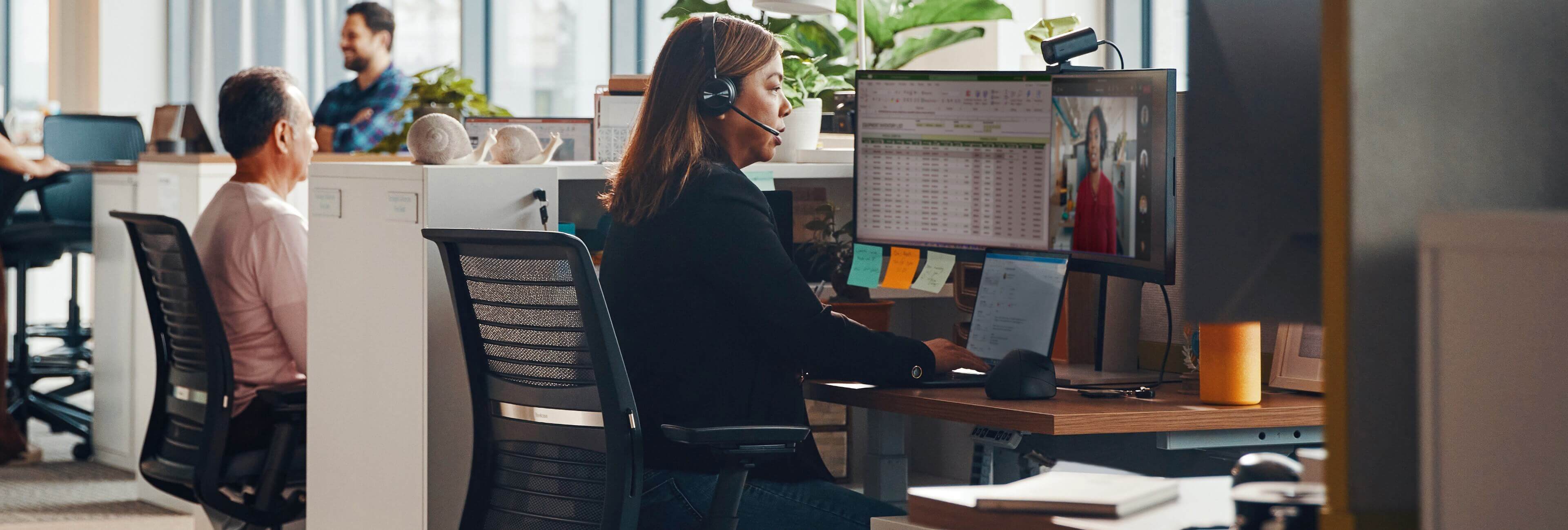 Businesswoman using a headset meeting online while sitting in front of two HP monitors.