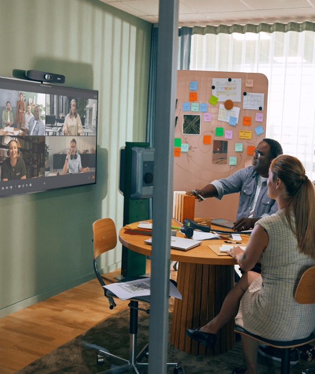 Team collaborating in small meeting room with colleagues on video call