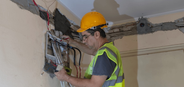 Electrical engineer finishing wiring connections with cables pulled through the walls by an electrical cable puller robot